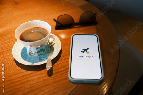 Obraz na plátne Smartphone displaying a flight delay notification beside coffee and eyeglasses on a table, illustrating travel disruption, changing plans and passenger inconvenience