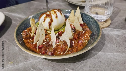 Cutting open a cheese ball dumpling in chili sauce Savory spicy tomato dip topped with creamy ice cream, crisp tortilla chips, pomegranate seeds, and sweet sauce in a ceramic bowl.