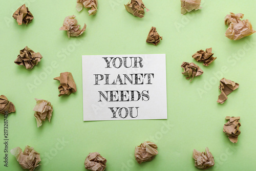 Obraz na płótnie A card with the message 'Your Planet Needs You' surrounded by crumpled paper on a green background, emphasizing environmental awareness and waste reduction