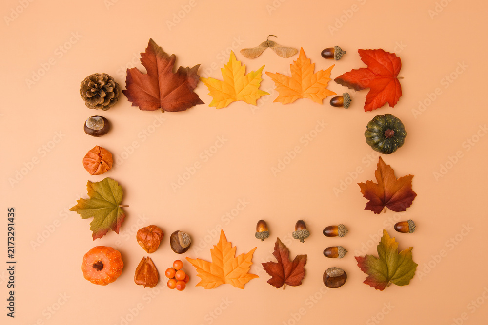 Fototapeta premium Autumn frame made of colorful maple leaves, acorns, pine cone and miniature pumpkins on a warm peach background, photographed from directly above. Seasonal composition with generous copy space.