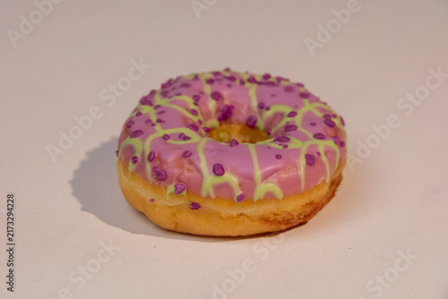 Cuadro en lienzo Bright pink donut with purple and green icing placed on a plain background