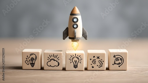 Toy wooden rocket launching off line of wooden blocks printed with lightbulb and creative icons.