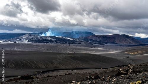 Volcanic ash fields with smoke plumes rising from distant mountains under a cloudy sky
