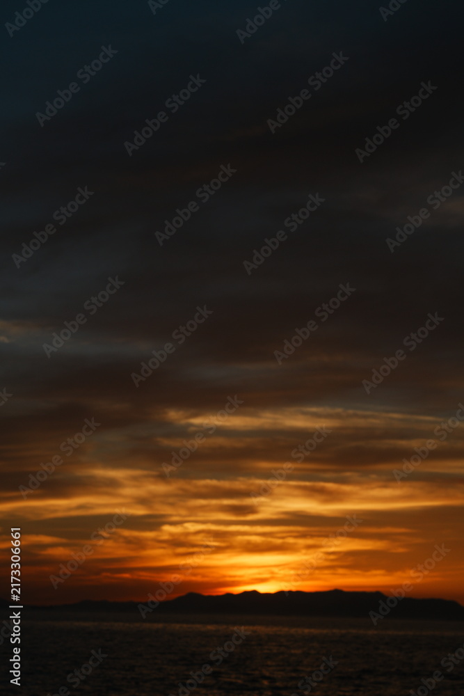 Fototapeta premium 夏の瀬戸内海で日没後に厚い雲の下へ橙色が残る夕焼けの空と山並み