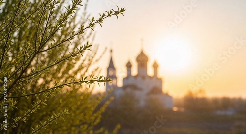 Spring landscape with willow branches in foreground and blurred orthodox church silhouette at sunset

