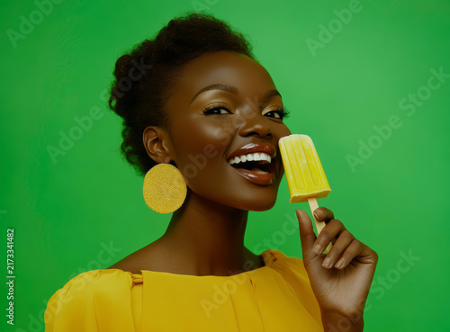 Woman smiling with yellow popsicle on green background