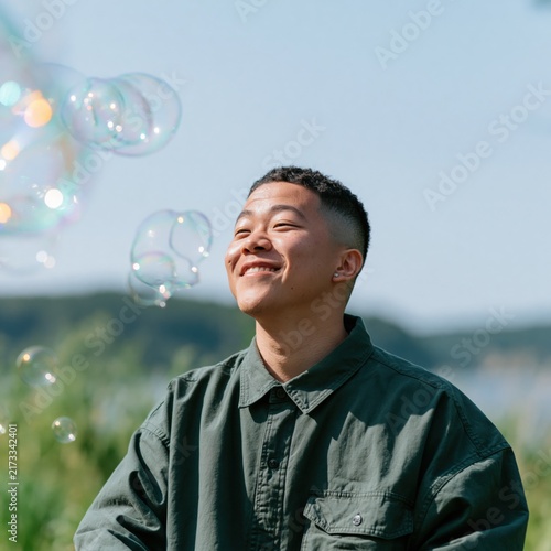 Smiling young man enjoying soap bubbles outdoors near water for relaxed summer background and lifestyle content