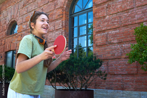 Teenager plays table tennis outside a brick building