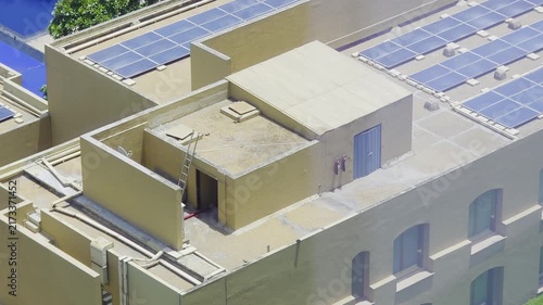Pan up reveal aerial drone shot rooftop solar panels above an exotic Indian resort featuring lush trees, bright blue pools, and distinctive architecture.