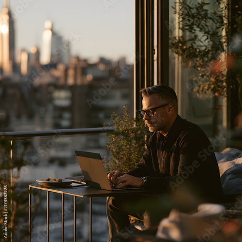 Businessman Working on Laptop Outdoors with Cityscape View at Sunset in Urban Environment