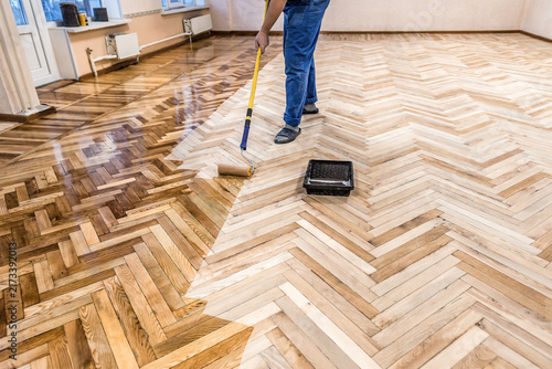 Quadro su tela Worker applying protective varnish layer on wooden herringbone parquet floor with a long handle roller