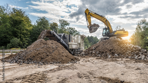Obraz na plátně Wide crop 16:9 of yellow excavator loading rocks into mobile crushing plant