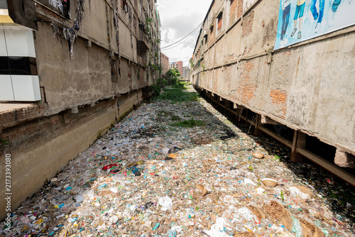 Dhaka, Bangladesh - 25 July 2023: View of plastic pollution clogging a narrow urban canal between weathered concrete buildings.