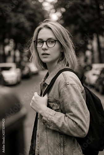 Young woman wearing glasses and a backpack walking outdoors in an urban neighborhood