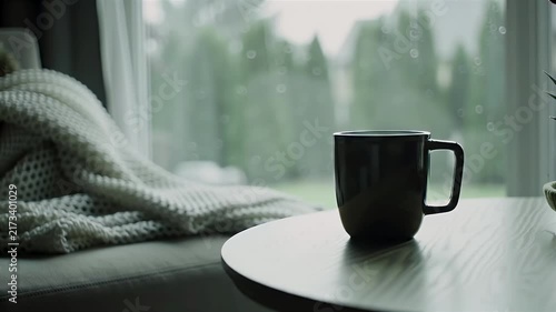 Black coffee mug on table with cozy knitted blanket by rainy window for home relaxation