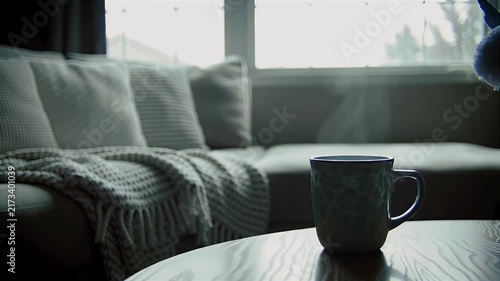 Steaming mug of hot coffee on a wooden table in a cozy living room with soft lighting.