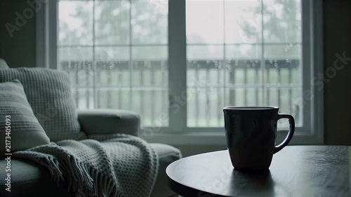 Coffee mug on table by window with cozy sofa and blanket in a rainy day living room
