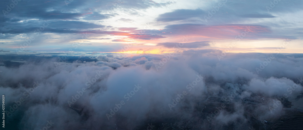 Obraz premium Aerial view above dramatic clouds in the Icelandic highlands at sunset, with soft golden light, misty valleys and a vast remote landscape hidden beneath the clouds.