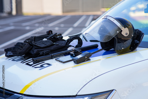 Fotografía Police tactical equipment including a riot helmet, baton, and vest laid on the hood of a patrol car