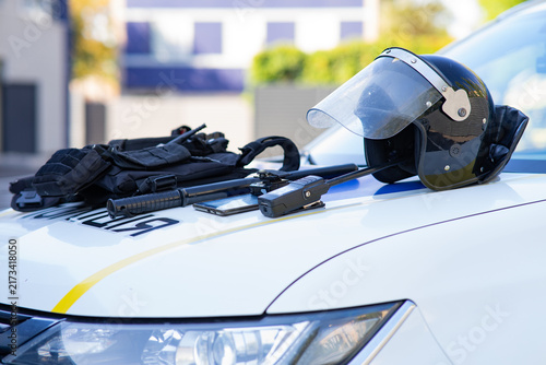 Fotografía Police tactical equipment including a riot helmet, baton, and vest laid on the hood of a patrol car