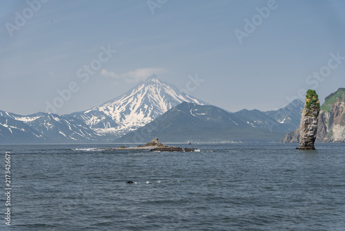 Bild auf Leinwand Sea stacks rise from Avacha Bay with snow-covered volcano and mountain coast across Kamchatka, Russia