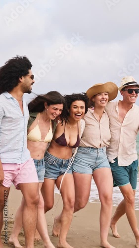 Diverse group of young friends walking and laughing on the beach together