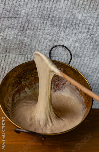 Stirring bread dough in an old brass bowl with a wooden spoon. Rustic charm, traditional baking.