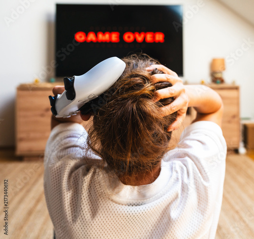 Fotografie Female gamer reacting to losing a video game as TV screen displays “Game Over”