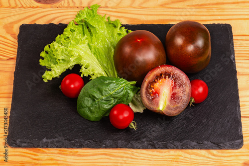 Reddish brown and red cherry tomatoes, greens on slate plate