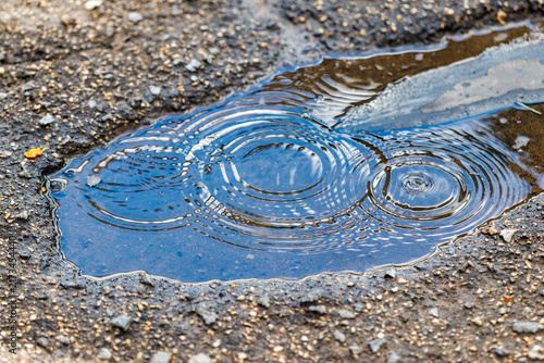 Fotografie Ripples form in a shallow puddle on cracked asphalt