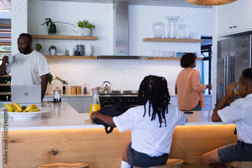 African American family preparing breakfast at kitchen island with orange juice backpack and laptop