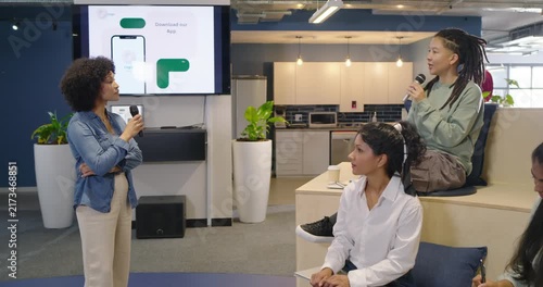 Diverse team watching host demoing app at office, sparking questioner asking into mic, copy space