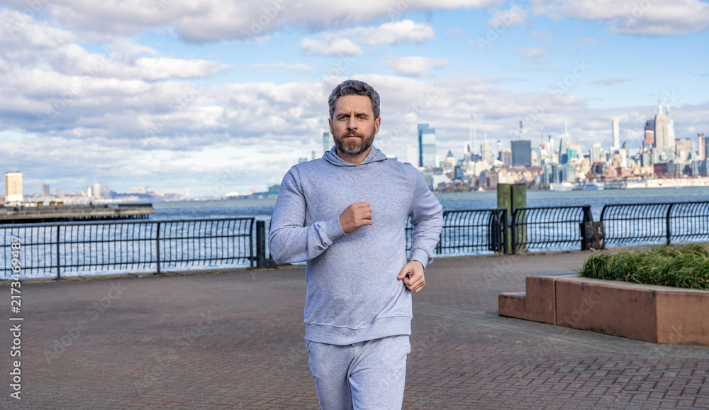 Fototapeta premium Sportsman jogger running or jogging. Man in sports suit training jogging. Running man in Manhattan. Male jogger. Morning sport workout jogger run in New York. Jogger run at sport training outdoor