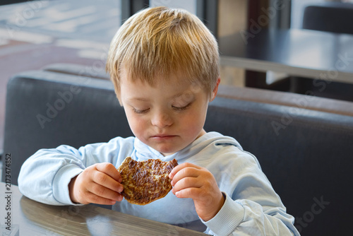 Konstfotografi Boy with Down syndrome eating a homemade meat patty at a table, childhood nutrit