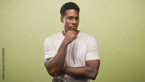 Fotografie Man with hand on chin and crossed arms in studio green backdrop wearing t shirt; contemplative reflection