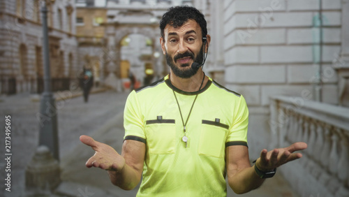 Fotografie Man referee in neon yellow uniform beckons with open hand and whistle on a historic street promenade; authority