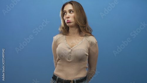 Фотография Woman pouting lips, wearing beige sweater and belt, hands held behind back in studio; quiet disappointment