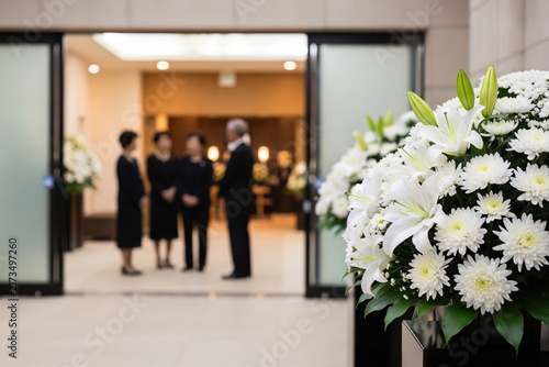 斎場に飾られた白百合の供花と喪服姿で参列する遺族・親族の葬儀・法要風景