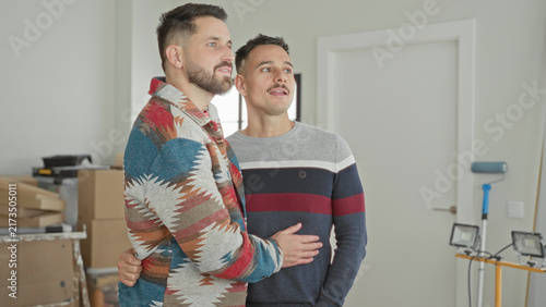 Foto Two men embrace with hand on waist beside moving boxes and a paint roller in a building; new home joy