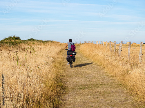 Hombre en una bicicleta por el campo amarillo hacia el horizonte azul en Etretat la Normandía Francesa. Viajando en verano de 2022