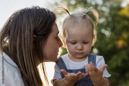 Mother whispers a secret to her curious toddler in a sunlit outdoor setting