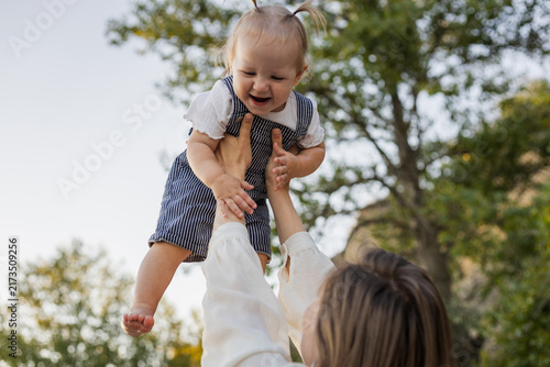 Joyful mother tossing her happy baby in the air outdoors on a sunny day