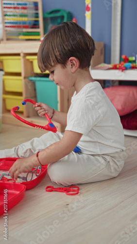 Obraz na plátně Boy playing with red toy stethoscope, puts stethoscope to ear in building playroom; curiosity imagination