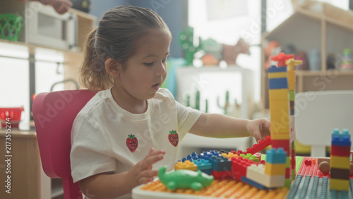 Принти на полотні Hispanic girl stacking colorful toy blocks with hand, constructing a tower in a building; concentration learning creativity
