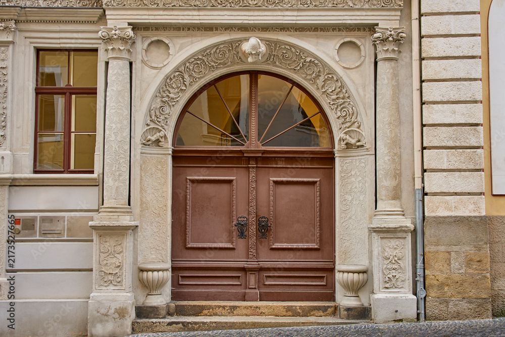 Naklejka premium Large wooden double door framed by detailed stone carvings, columns and arched window