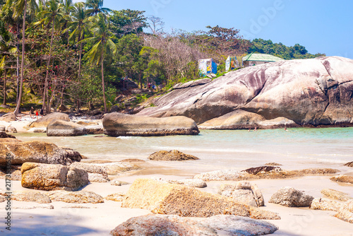 Bild auf Leinwand Scenic rocky coastline with massive boulders on a sandy beach below a jungle hill