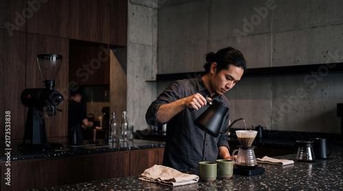 Asian male barista carefully pouring hot water from a black gooseneck kettle into a filter dripper to brew pour over coffee in a modern cafe