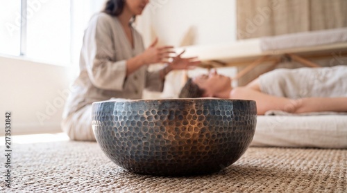 Tibetan Singing Bowl in Foreground with Energy Healer Performing Sound Therapy on Client in Background