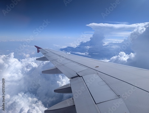 фотографія Airplane wing framed against a massive anvil-shaped cumulonimbus storm cloud building up in the bright blue sky during a flight
