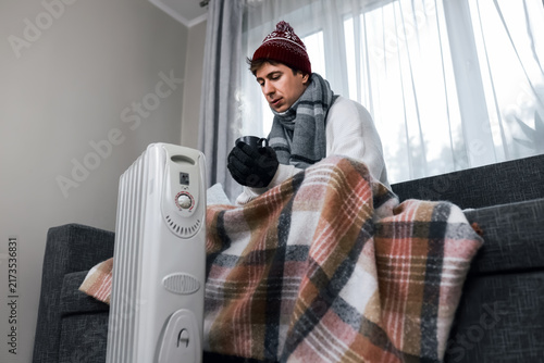 Cuadro en lienzo Freezing man indoors at home near a heater during a winter cold snap, facing ris